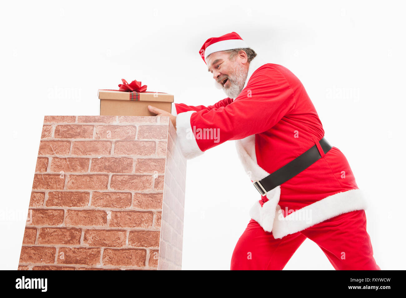 Side view of smiling Santa putting a present box into a chimney Stock Photo