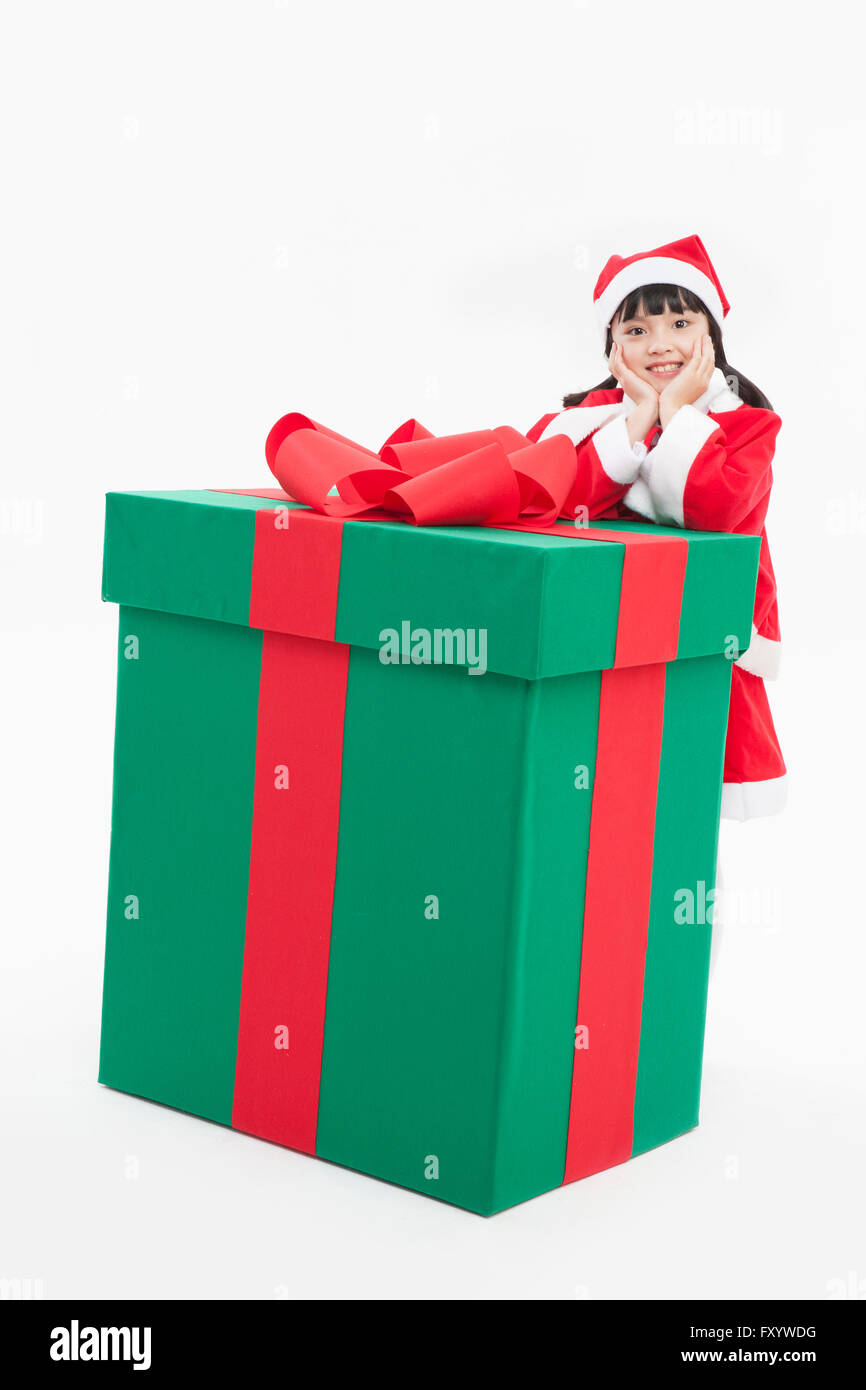 Smiling girl in santa's clothes posing with a big present box staring at front Stock Photo
