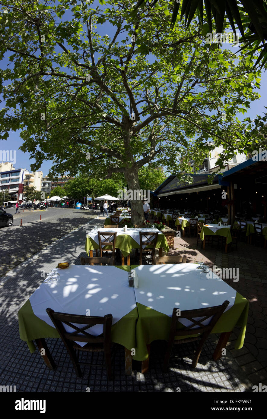 Close view of rows of empty restaurant tables, lined-up under the tree shade in Panagia district, Kavala city port bay, Greece Stock Photo