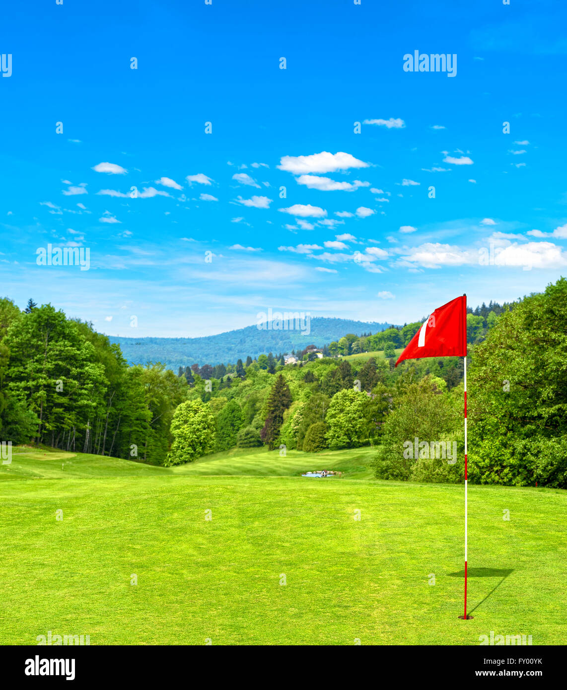 Green golf field and blue sky. Golf course with red flag. Spring landscape Stock Photo