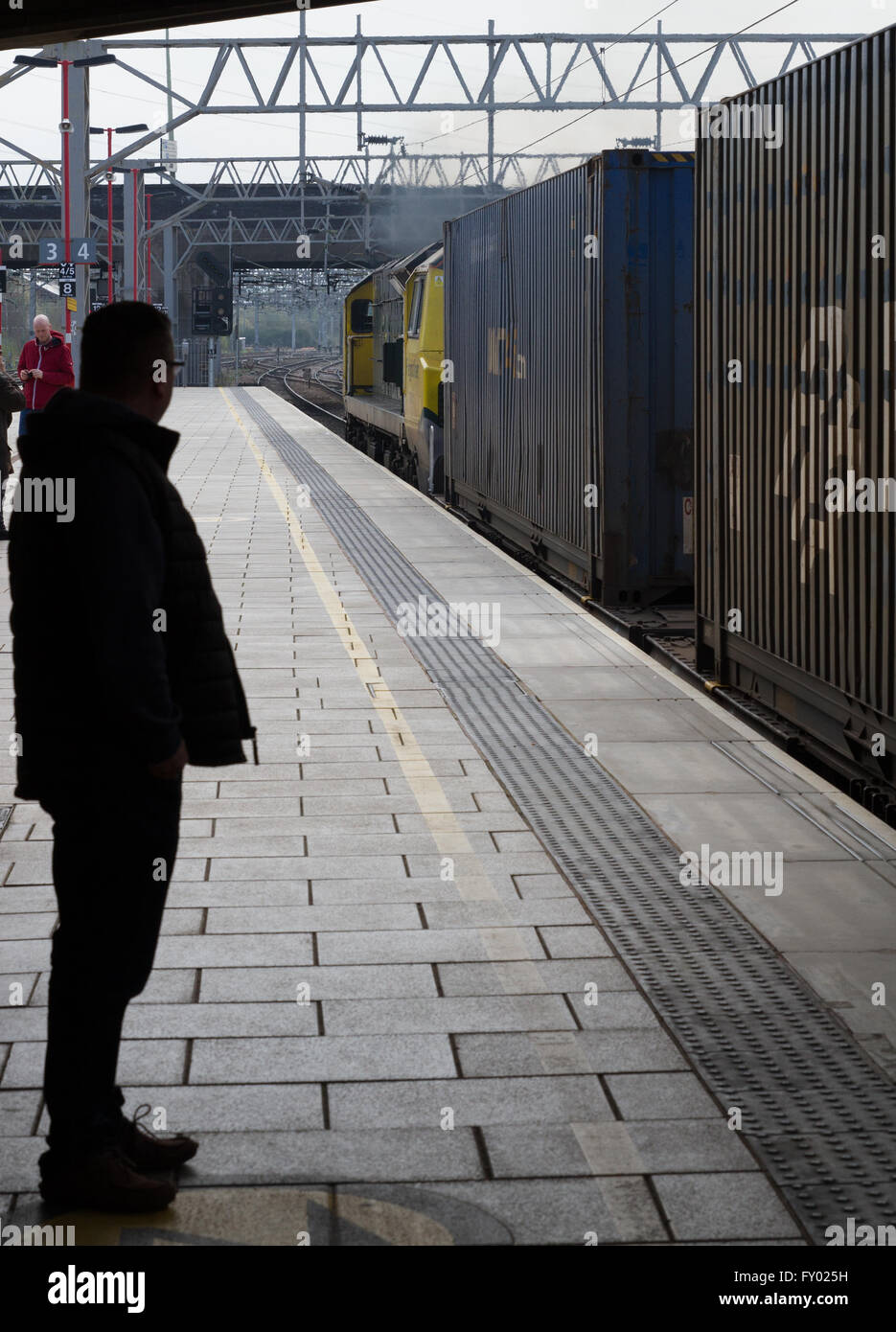 A passenger watches as a Freightliner Powerhaul Class 70 locomotive pulls a train of ISO shipping containers through Stafford. Stock Photo