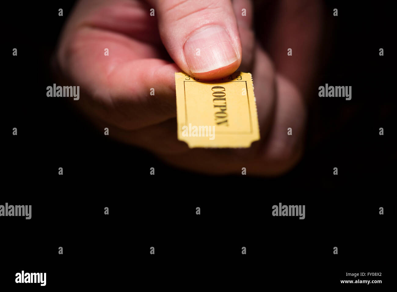 A man's right hand holding a yellow 7-digit ticket marked with the word 'COUPON' printed in black ink Stock Photo