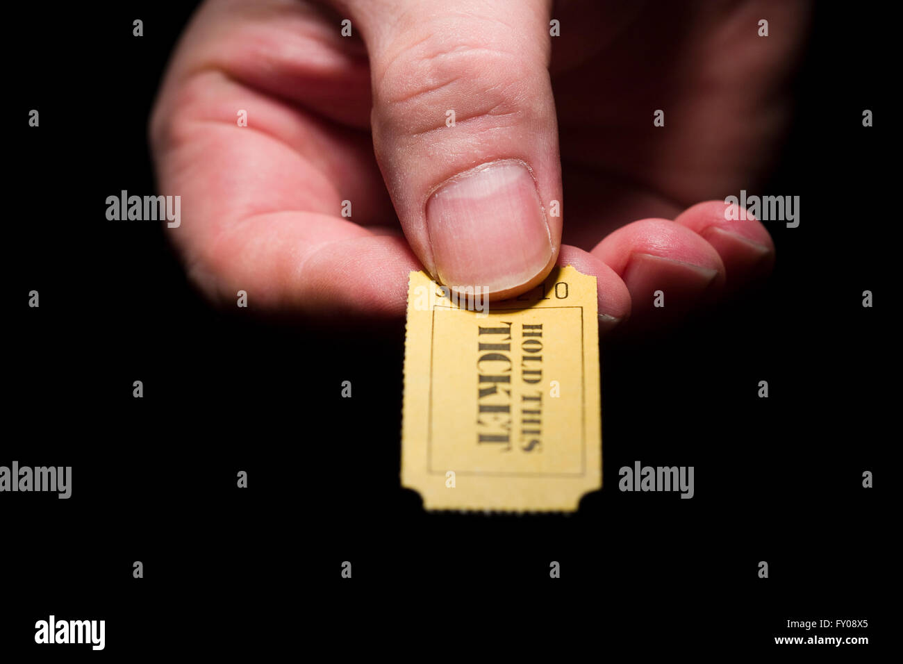 A man's right hand holding a yellow 7-digit ticket marked with the words 'HOLD THIS TICKET' in black ink Stock Photo