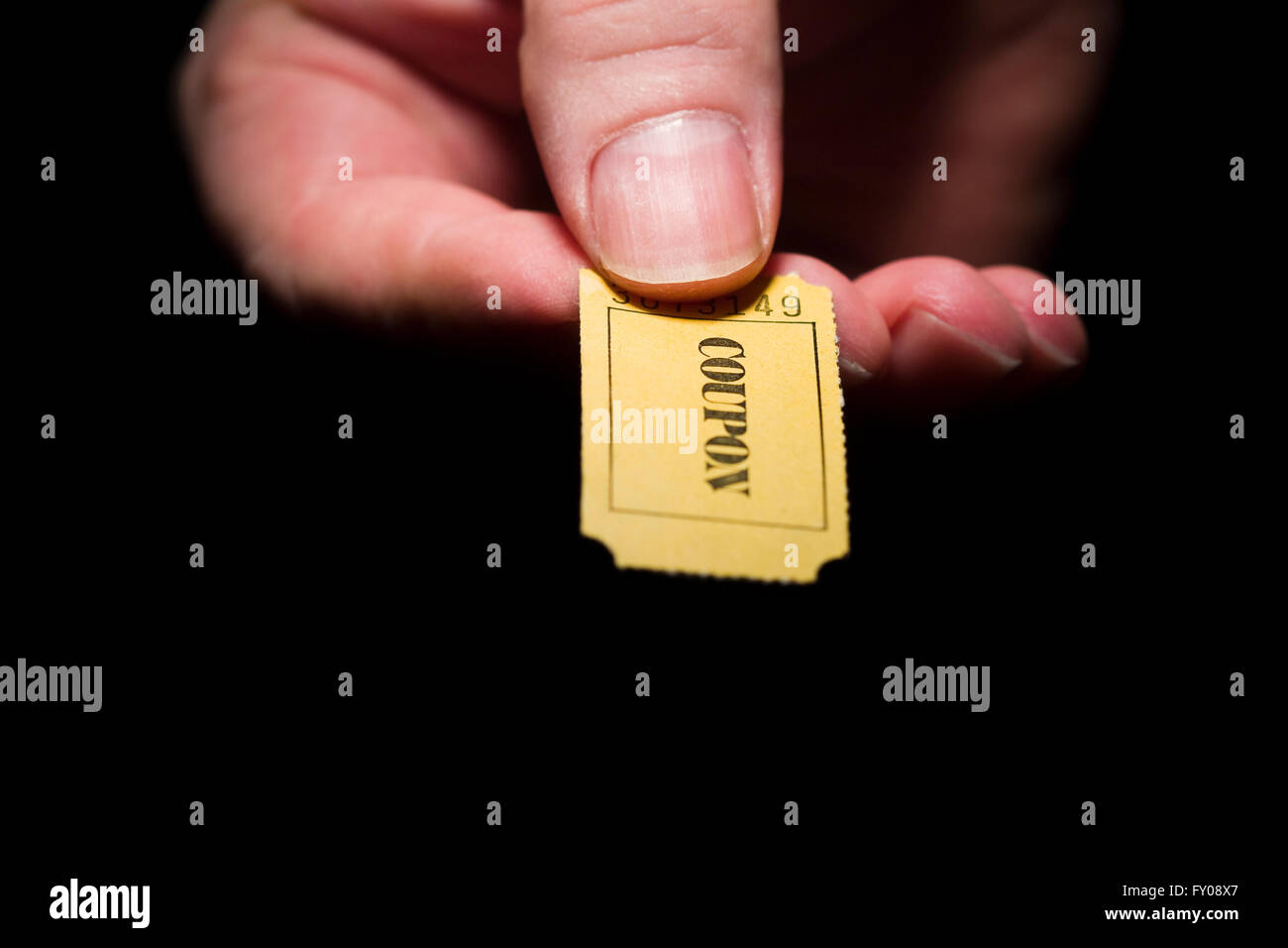 A man's right hand holding a yellow 7-digit ticket marked with the word 'COUPON' black ink Stock Photo