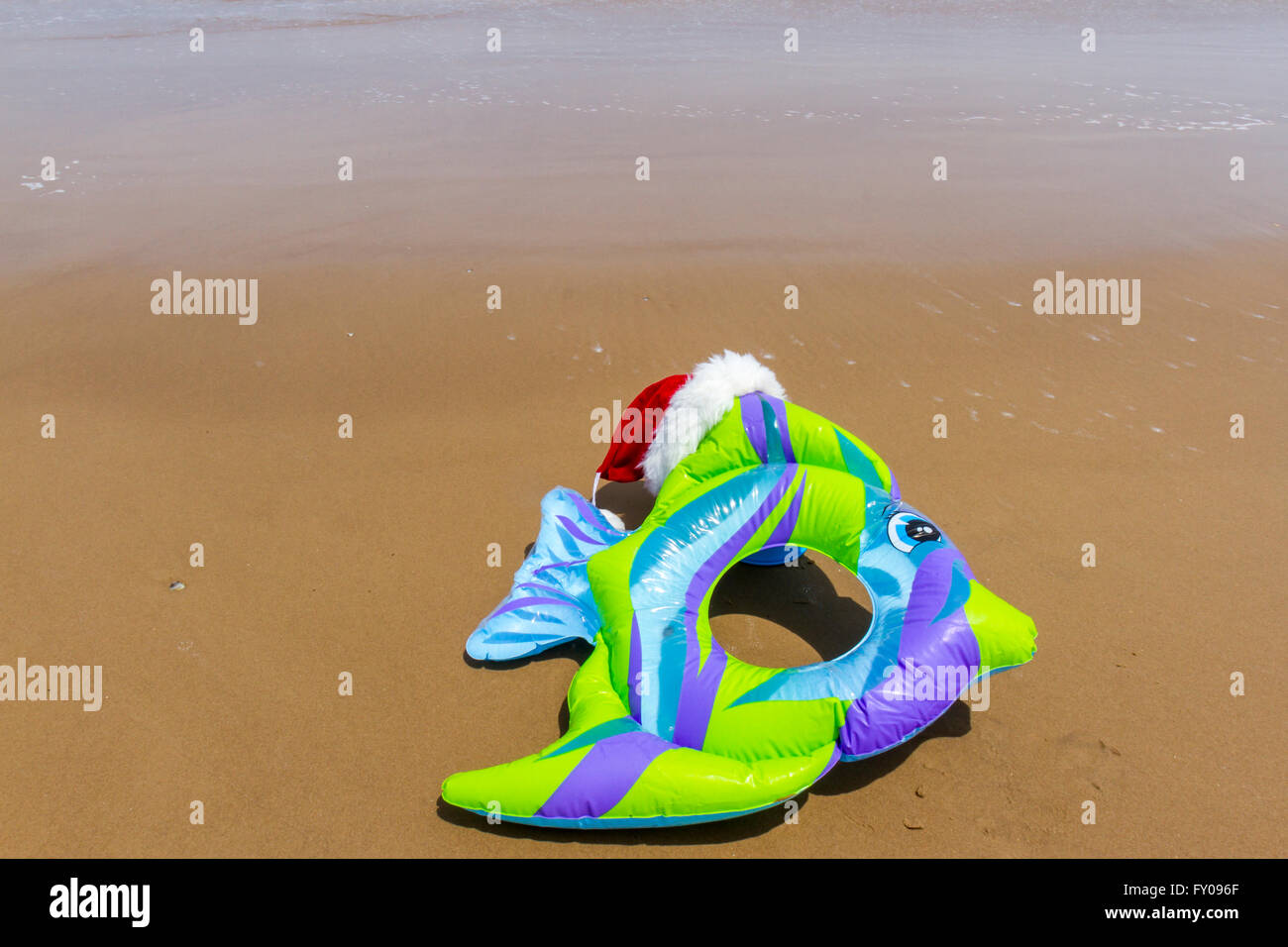 Inflatable kids fish beach toy wearing Santa hat on sandy beach. Stock Photo