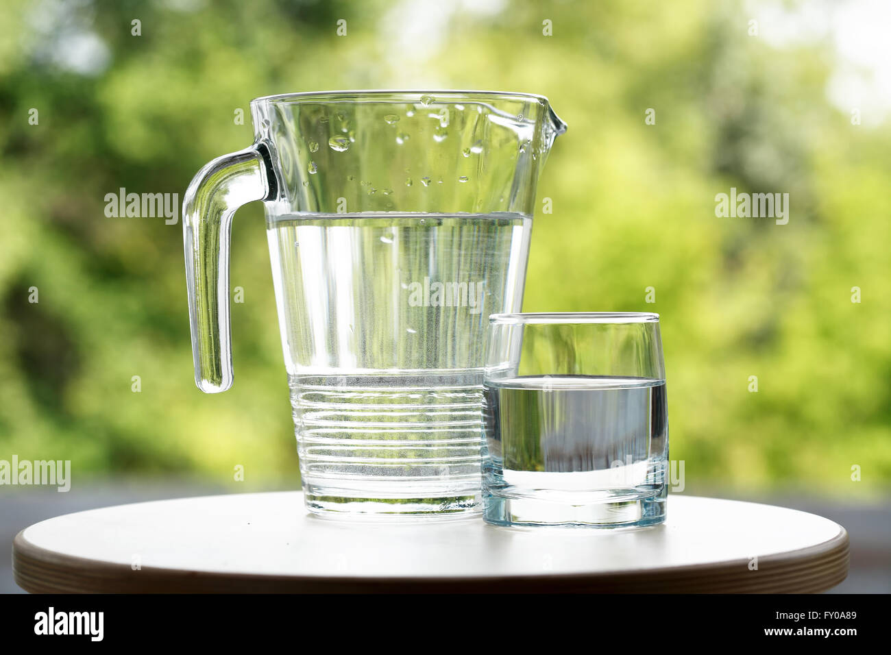 Glass of water near jug on green nature background Stock Photo