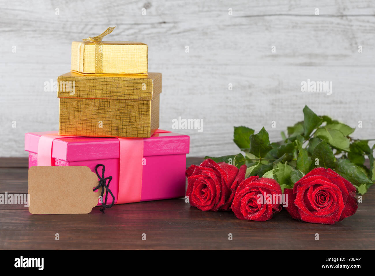 Three red roses and three gift boxes with empty tag on wooden table