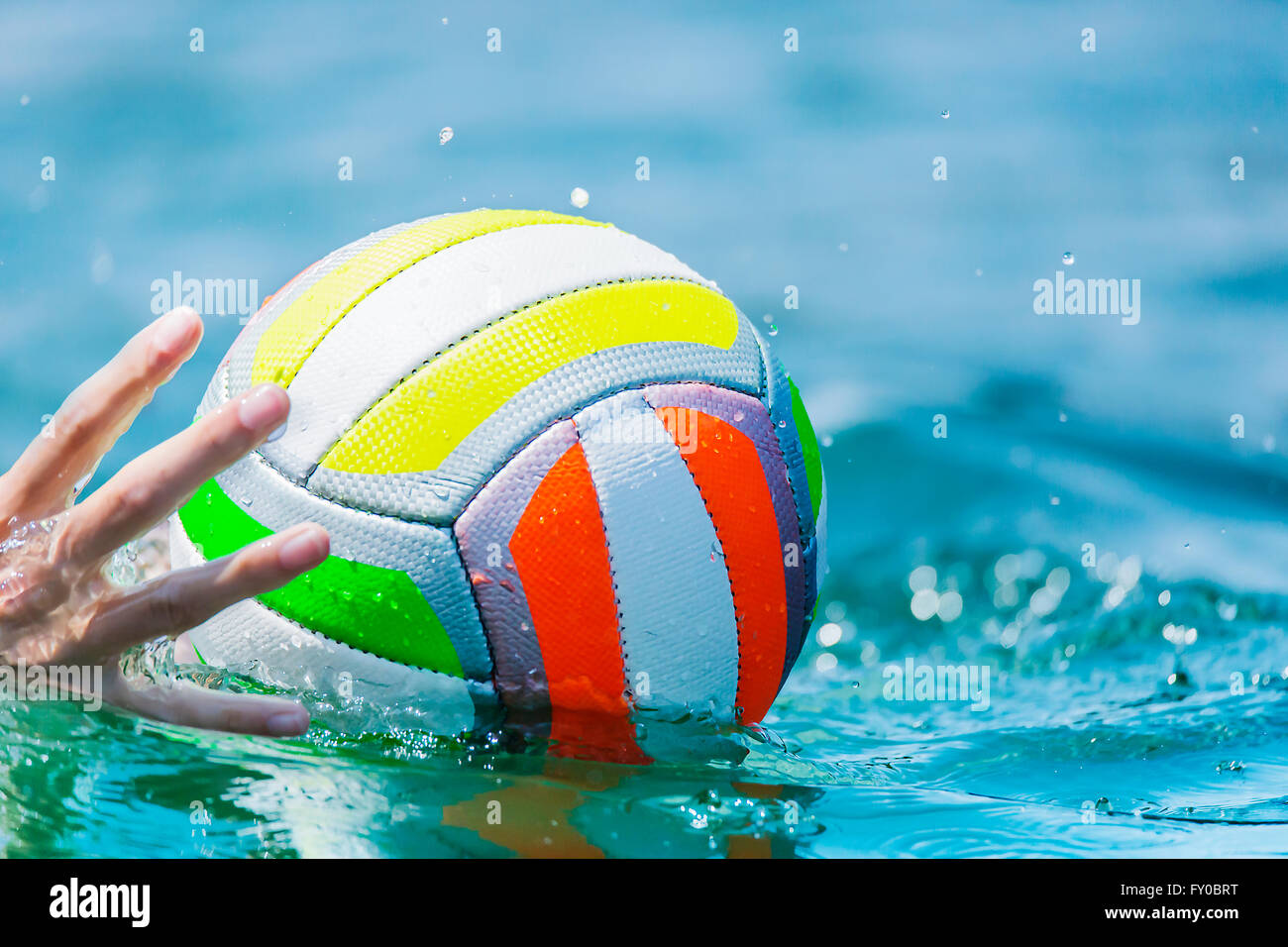 A hand of a swimmer reaches for a beach ball in the water Stock Photo