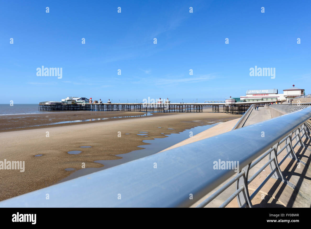 Under a bright blue sky, the view from the promenade across the sandy beach to North Pier in Blackpool, Lancashire Stock Photo