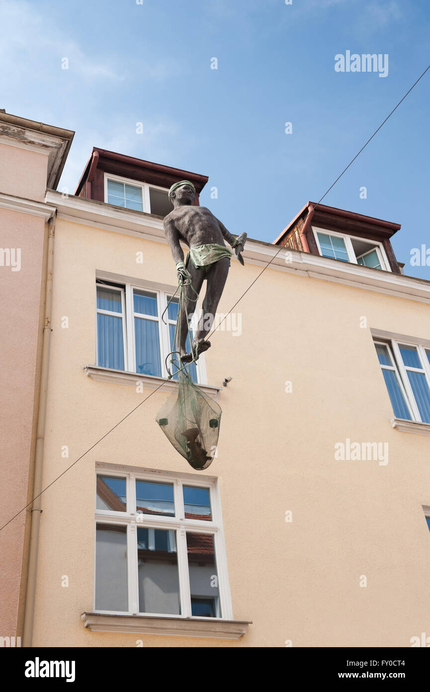 Tightrope walking fisherman sculpture, a walker balancing on the rope between two buildings exterior holding fish in the net. Stock Photo