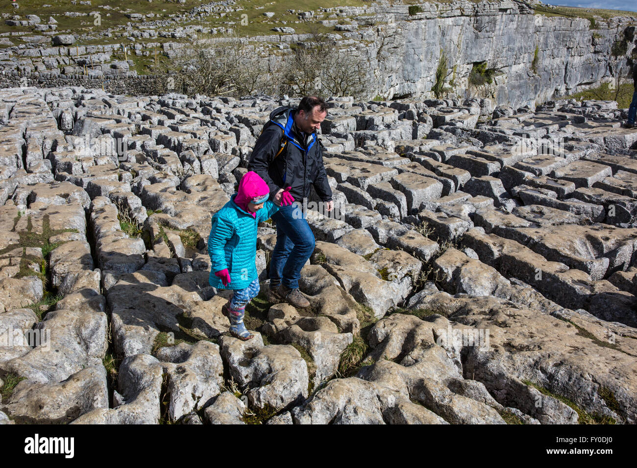 A man and his daughter navigate the limestone pavements on the cliff at Malham Cove in North Yorkshire, England Stock Photo