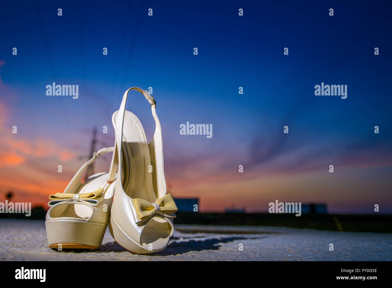 Bride white shoes on a rock with sunset behind Stock Photo