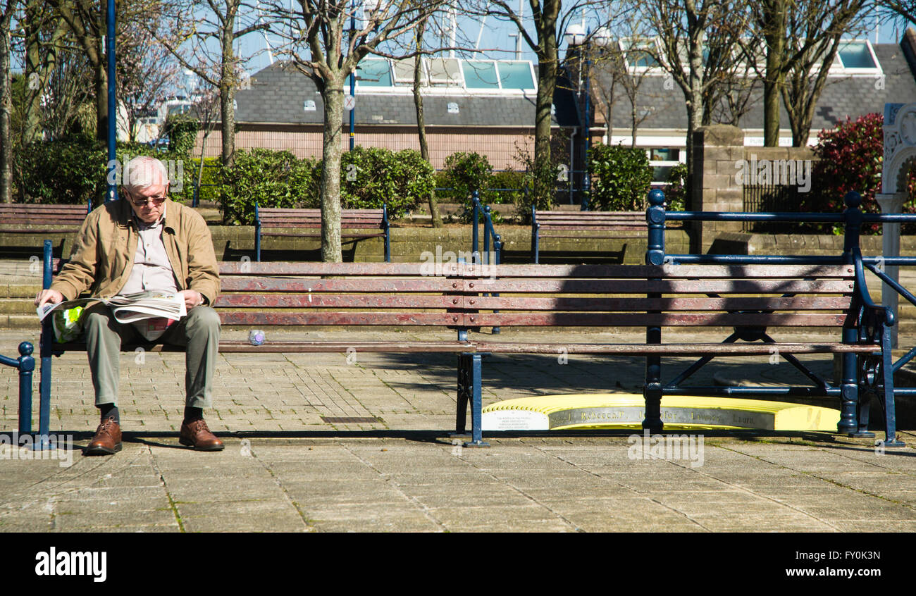 Elderly man sitting on park bench reading a newspaper Stock Photo - Alamy