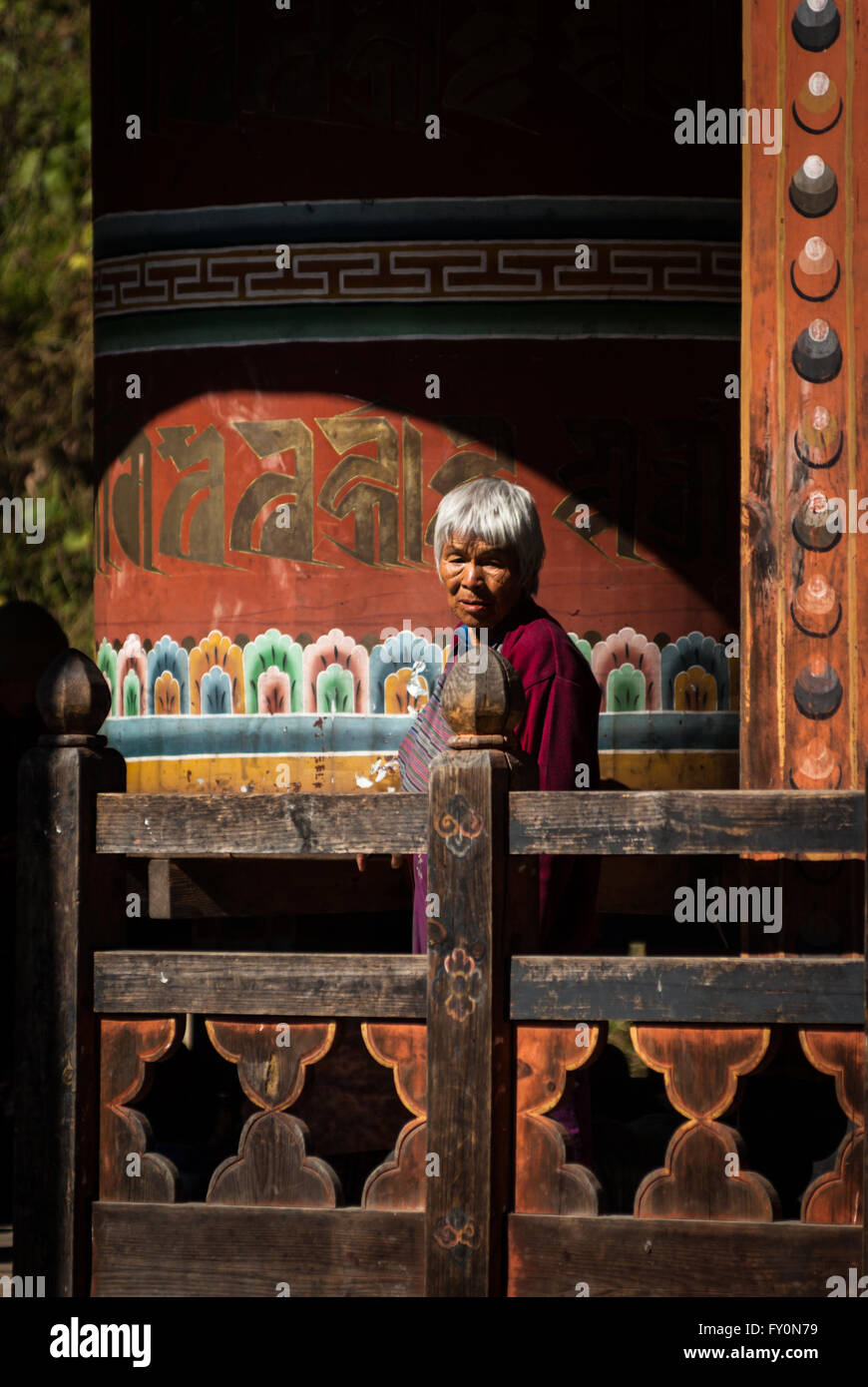 Elderly Bhutanese woman turning large wooden prayer wheel in Trongsa, Bhutan Stock Photo