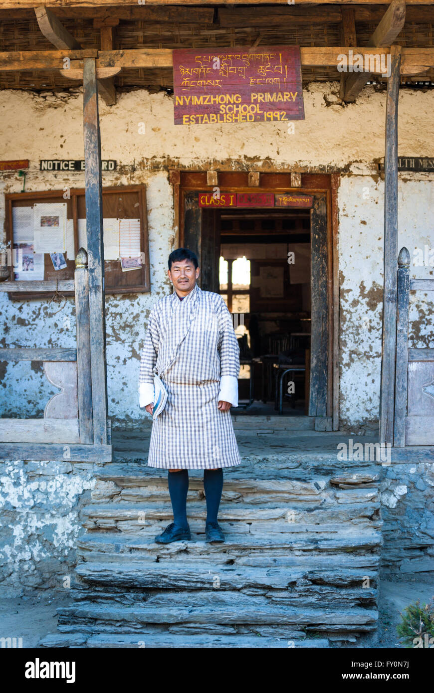 School principal wearing traditional gho standing on steps of dilapidated primary school in Nimshong vilage, Bhutan Stock Photo