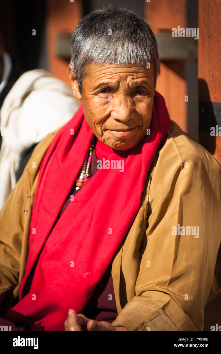 Elderly Buddhist nun sitting in sun on terrace at Paro Dzong, Bhutan Stock Photo