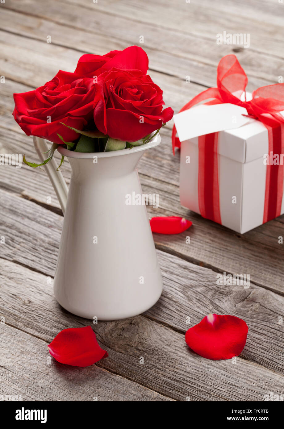 Red rose flowers in pitcher and Valentines day gift box on wooden table Stock Photo