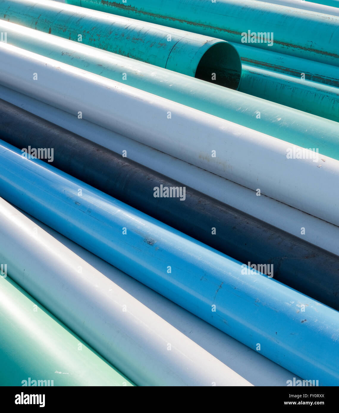 Abstract of blue, white and green water pipes stacked at a construction site on a sunny day Stock Photo