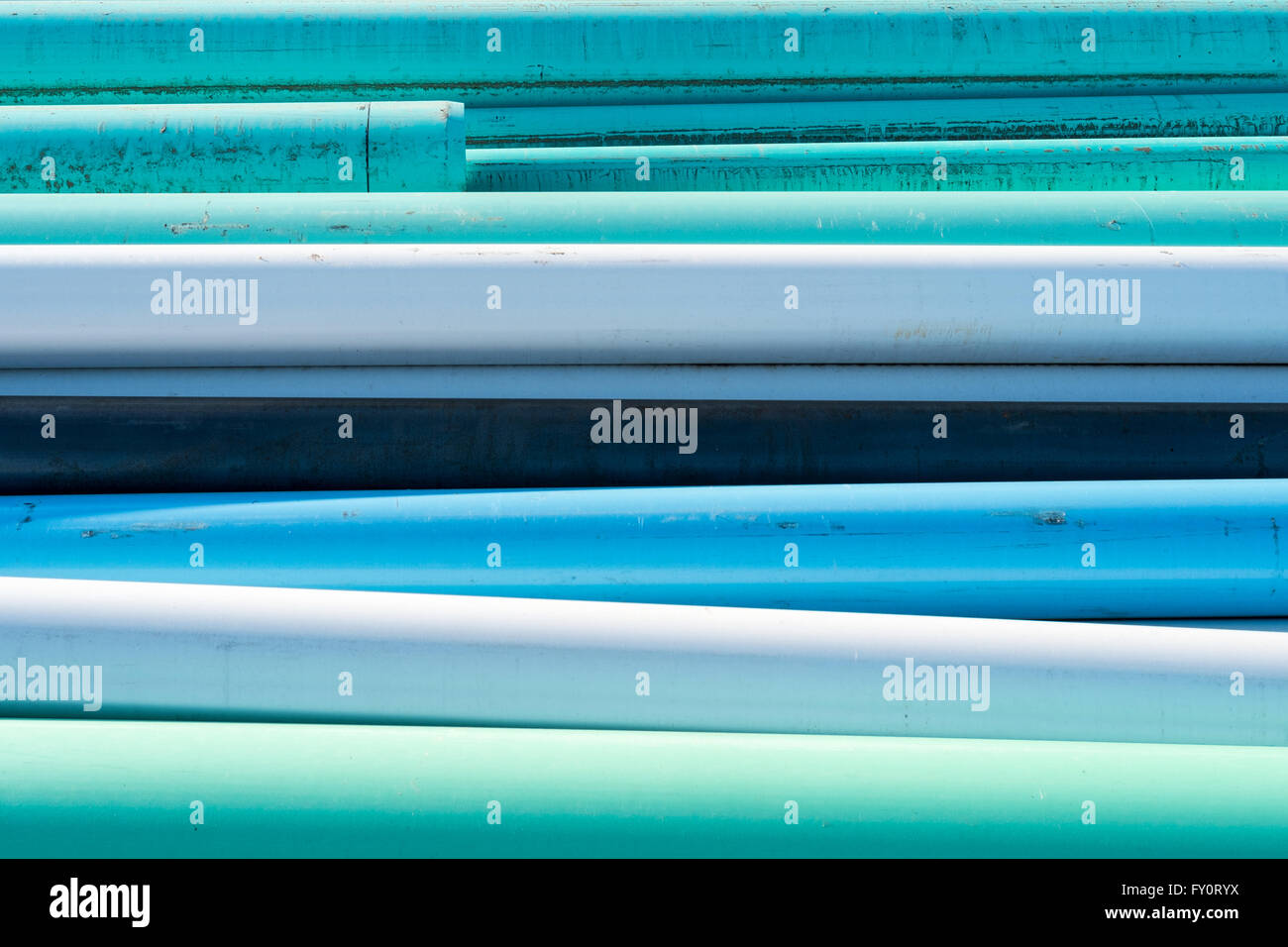 Abstract of blue, white and green water pipes stacked at a construction site on a sunny day Stock Photo