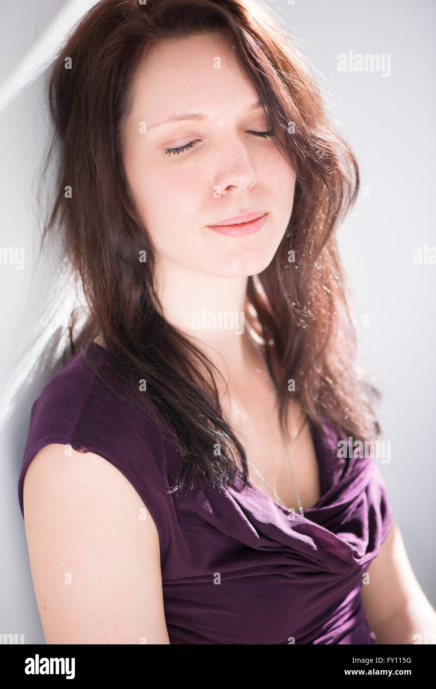 Woman sitting with eyes closed. Lifestyle image of young woman showing relaxation, contemplation and contentment. Stock Photo