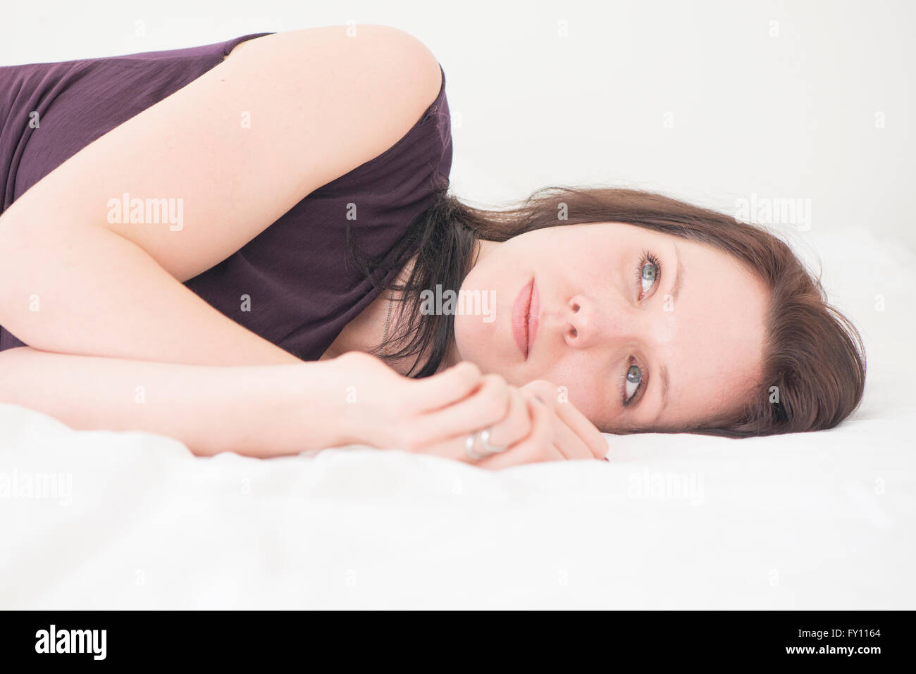 Portrait of young woman lying down in her bed resting. She is looking away with a serious and pensive expression. Stock Photo