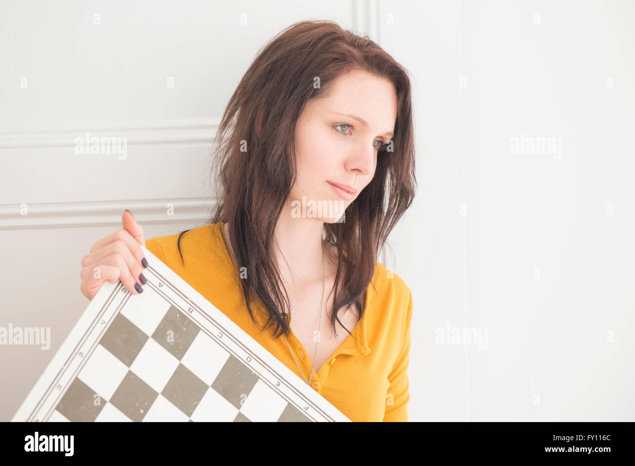 Serious woman holding chessboard in home interior. Concept of strategy, leisure activity and contemplation. Stock Photo