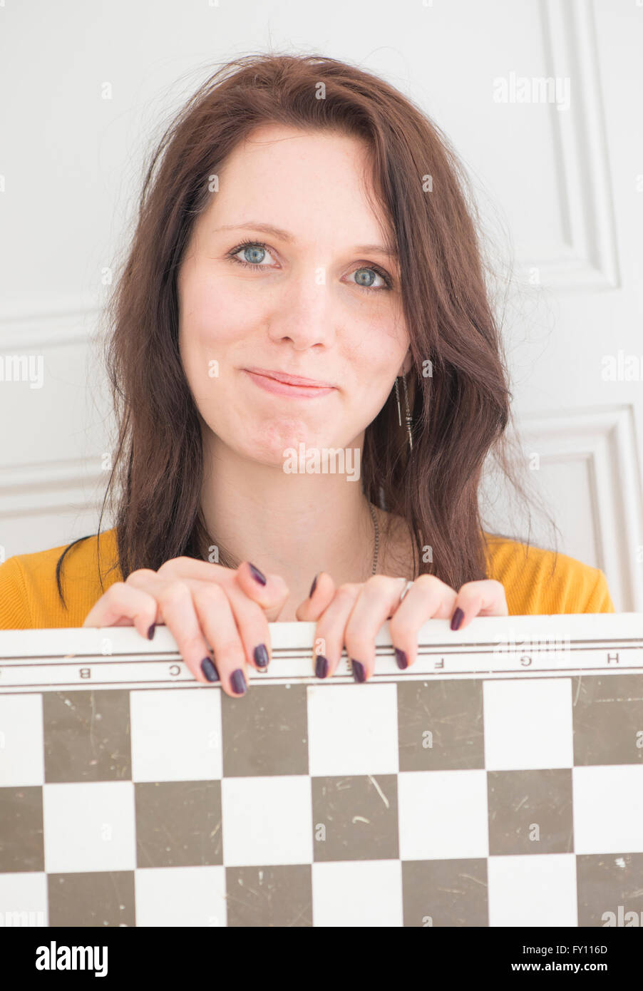 Smiling woman holding chessboard in home interior. Concept of strategy, leisure activity and playing games. Stock Photo