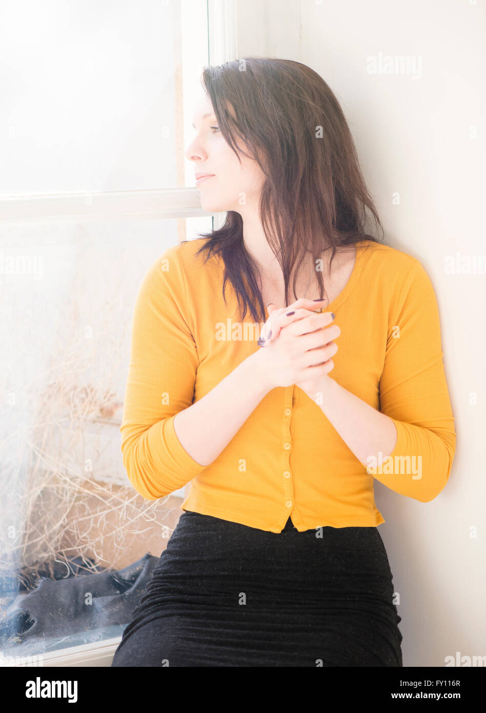Woman sitting by window, looking away. Lifestyle image showing a woman waiting and thinking. Stock Photo