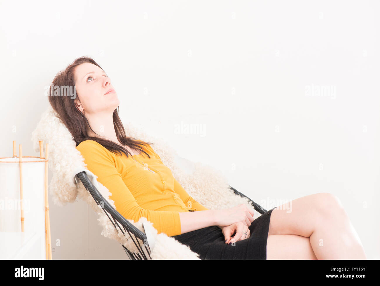 Woman sitting in chair, relaxing and staring at the ceiling. Concept of boredom, loneliness and contemplation. Stock Photo