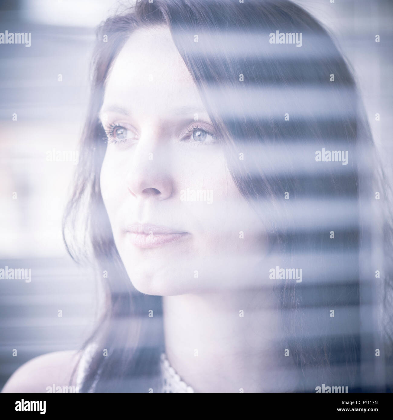 Woman standing by a window, looking away. Concept of sadness, waiting and anticipation. Lifestyle image of contemplation. Stock Photo