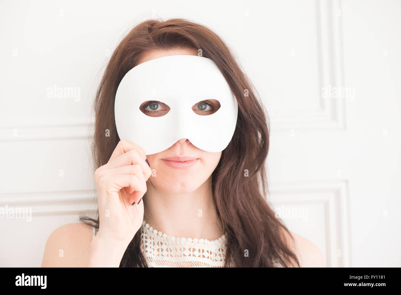 Woman hiding face behind white mask. Concept of identity, mystery, and disguise. Stock Photo