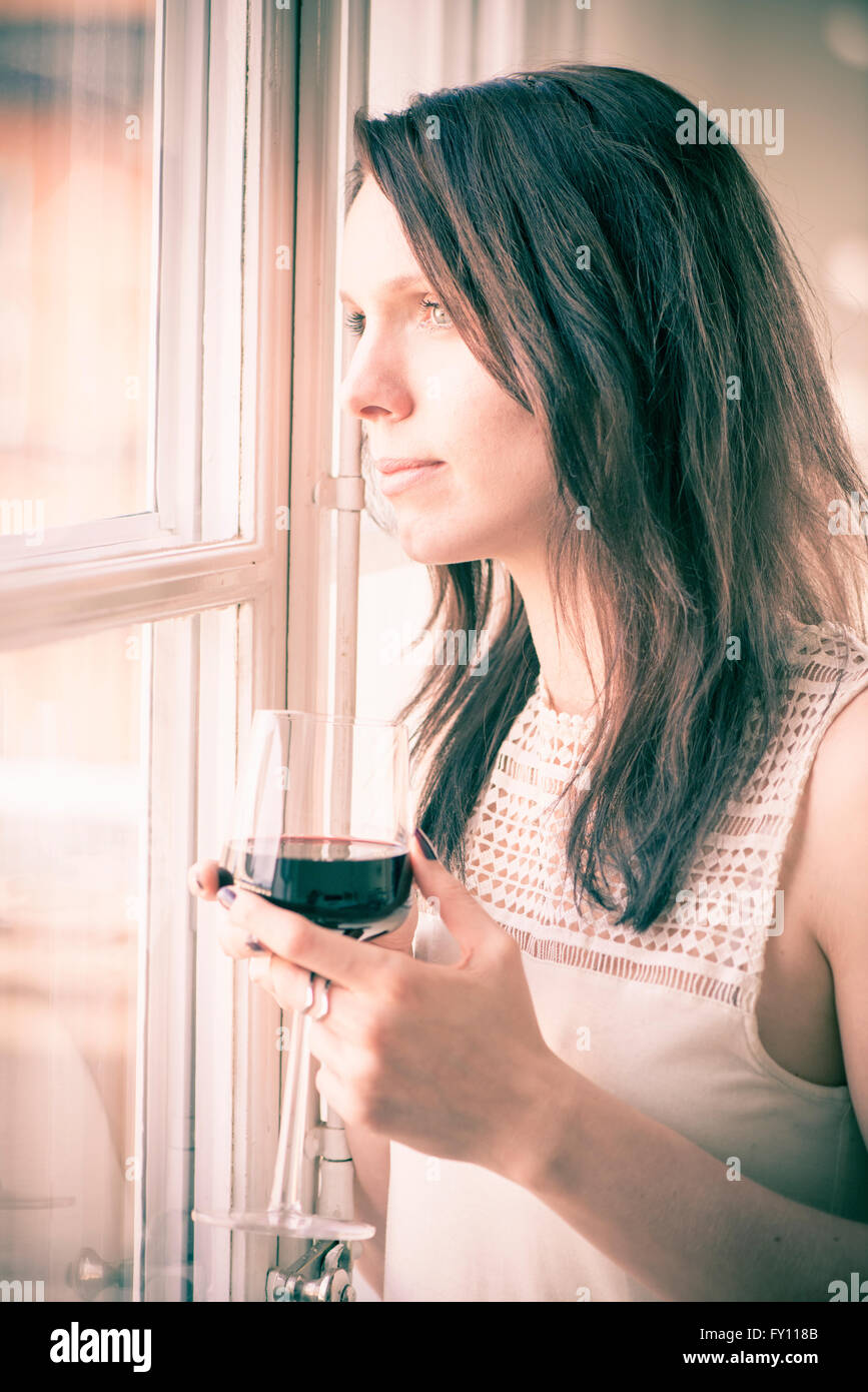Woman standing by a window, looking away. Concept of sadness, waiting and anticipation. Lifestyle image of contemplation. Stock Photo