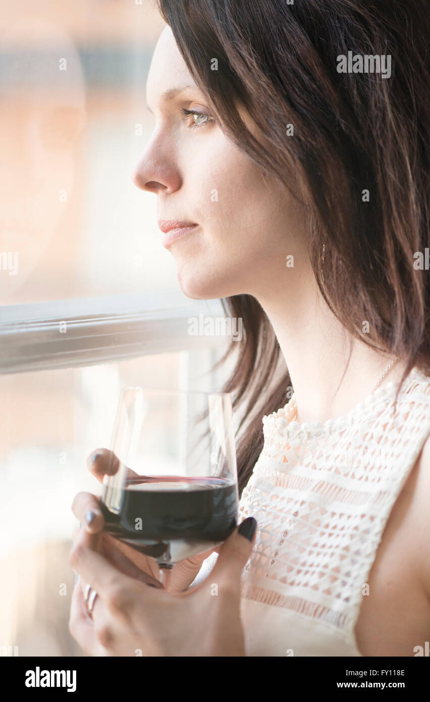Woman standing by a window, looking away. Concept of sadness, waiting and anticipation. Lifestyle image of contemplation. Stock Photo