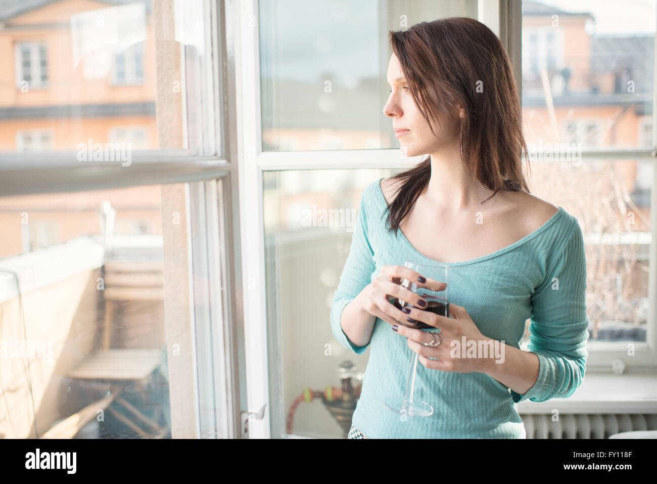 Woman standing by a window, looking away. Concept of sadness, waiting and anticipation. Lifestyle image of contemplation. Stock Photo