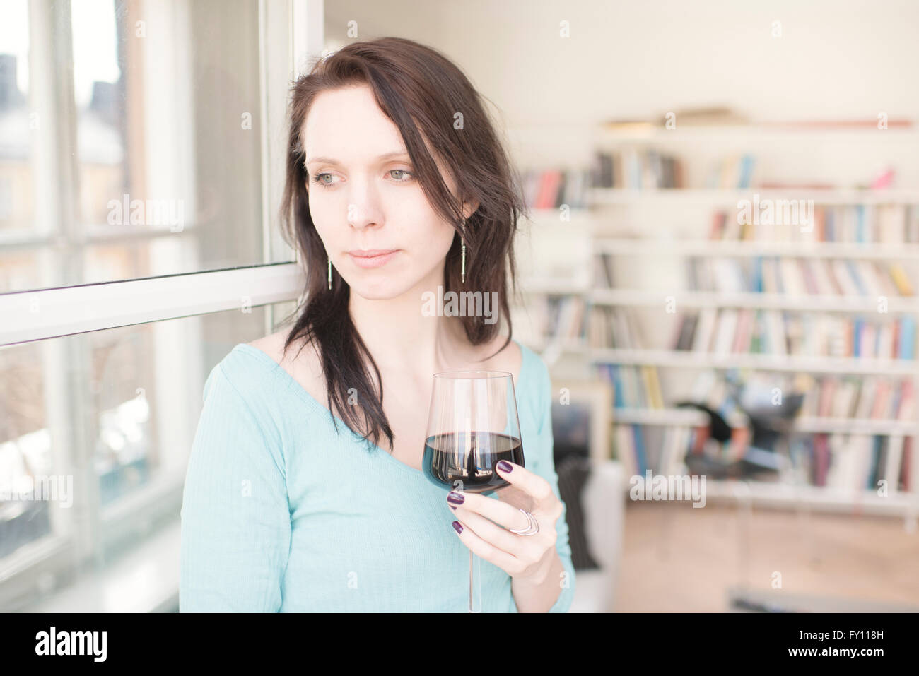Woman holding glass of red wine in home interior Concept of sadness waiting and anticipation Lifestyle image of contemplation. Stock Photo