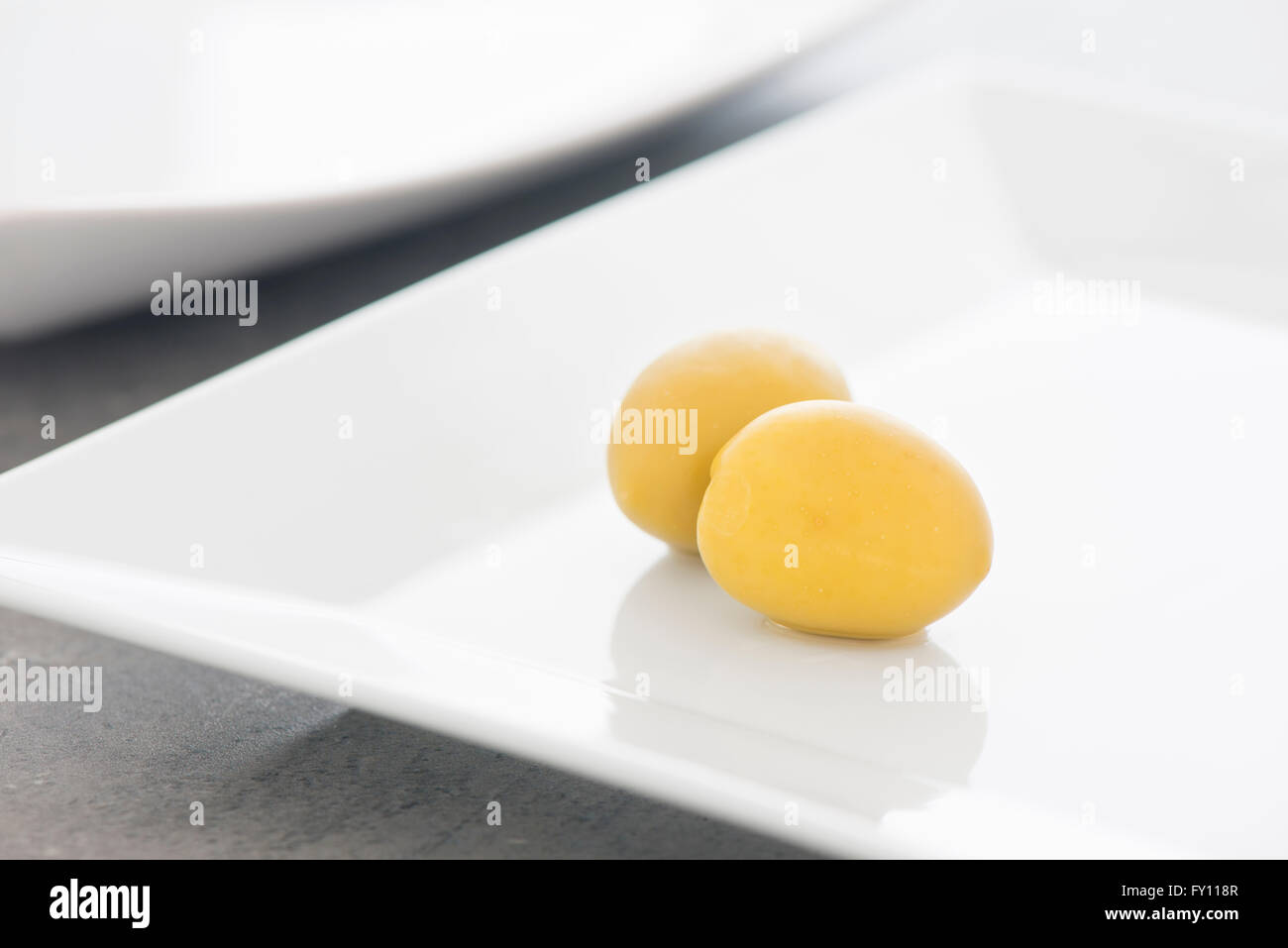 Green olives on white plate in close up. Still life photo of appetizer or snack. Stock Photo