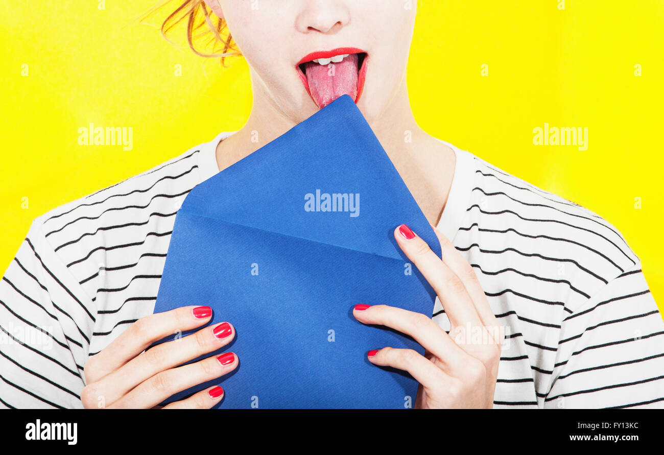 Midsection of woman licking blue envelope against yellow background Stock Photo
