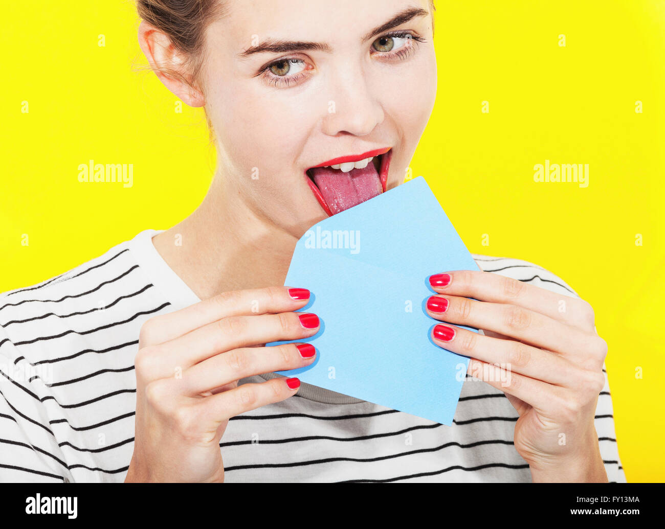 Beautiful woman licking blue envelope against yellow background Stock Photo