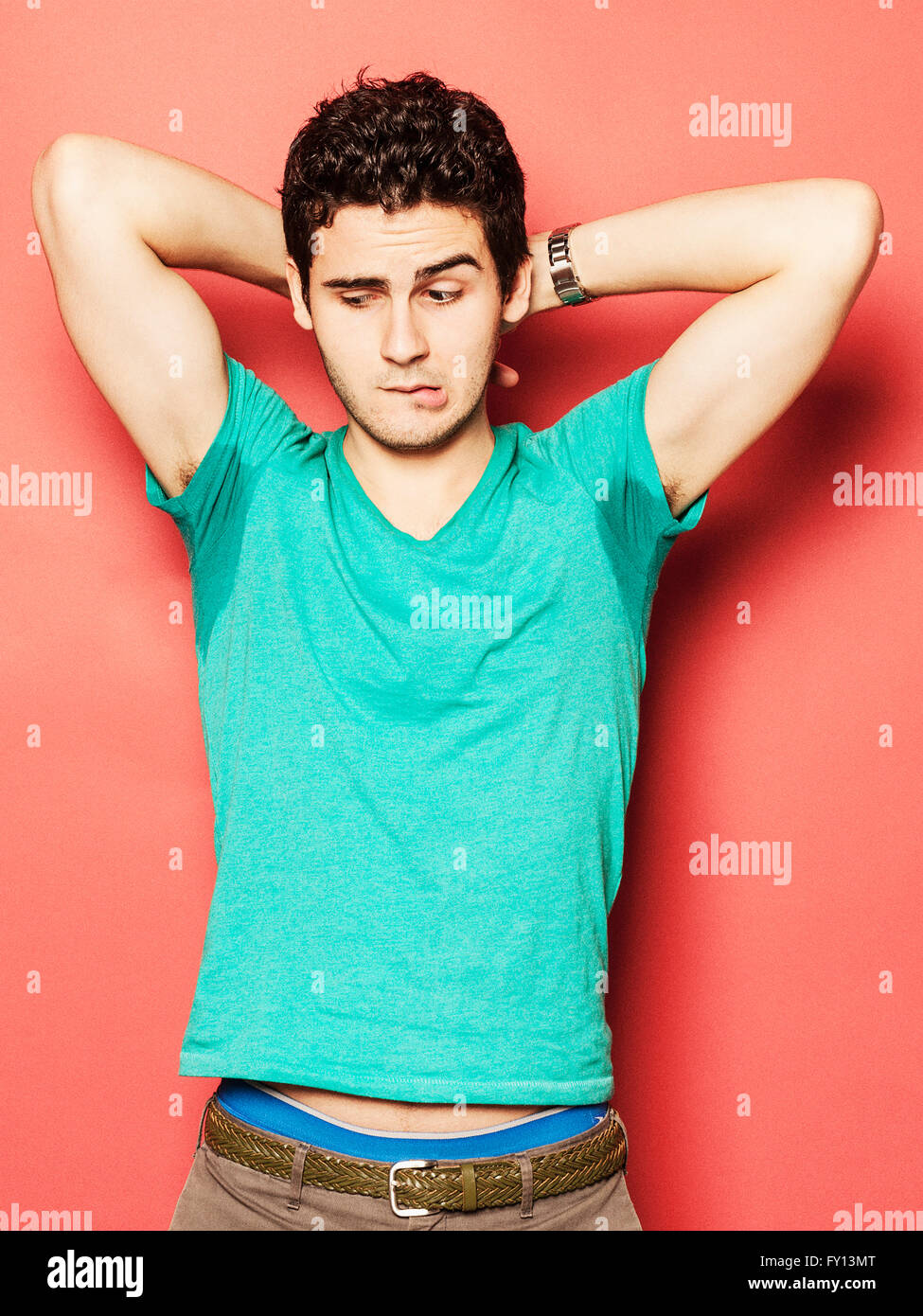 Young man biting lip while looking at sweaty armpit against red background Stock Photo