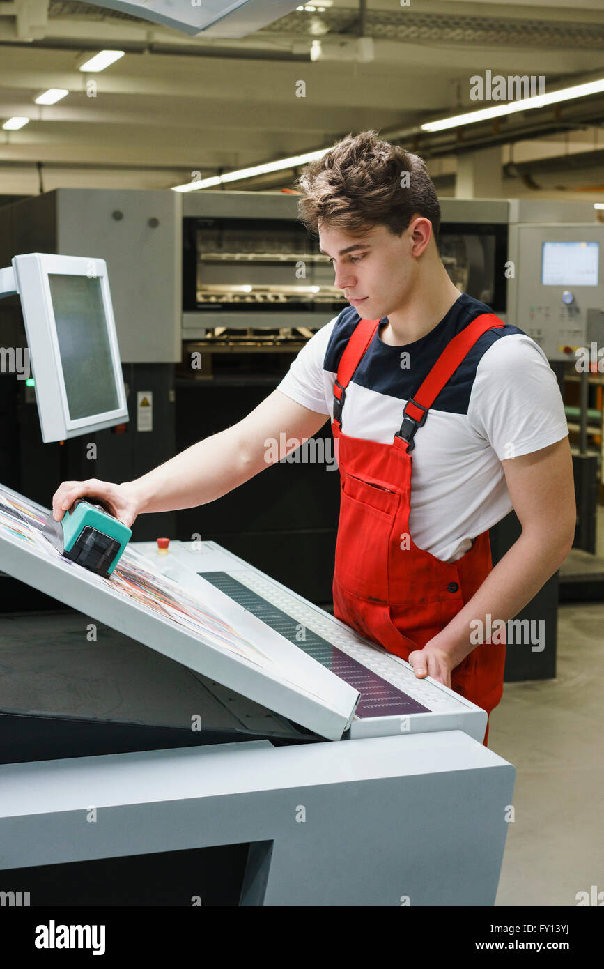 Young worker checking quality of printout with scanner at printing press Stock Photo