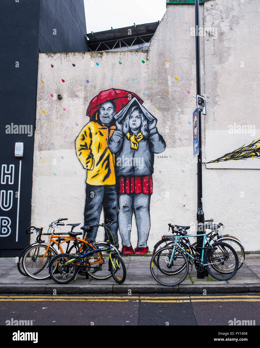 Big mural graffiti representing a surprised couple protecting from the rain with a red umbrella and a newspaper. Stock Photo