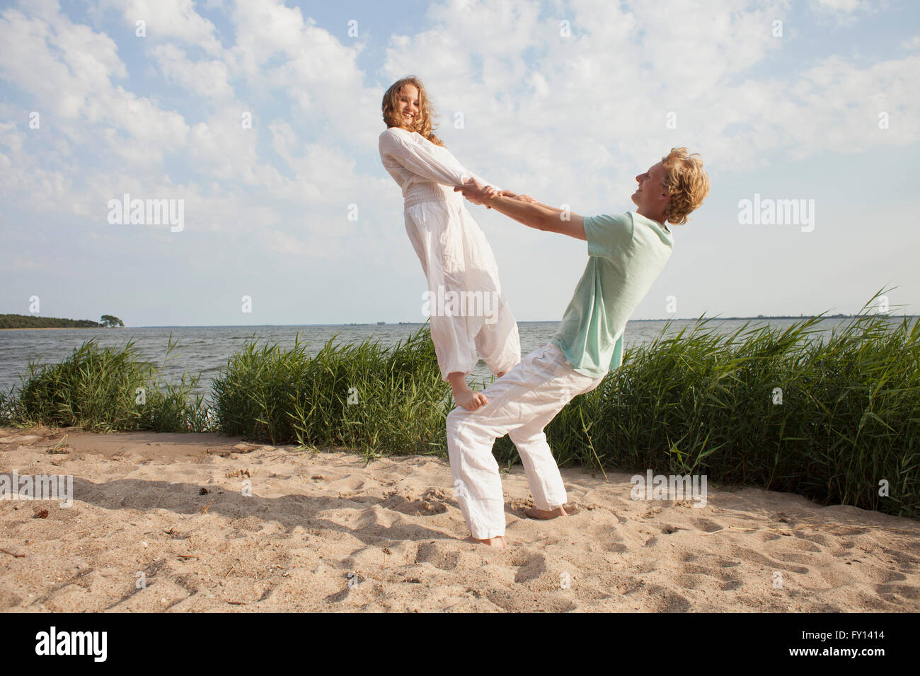 Woman balancing on friend's knee at beach against sky Stock Photo
