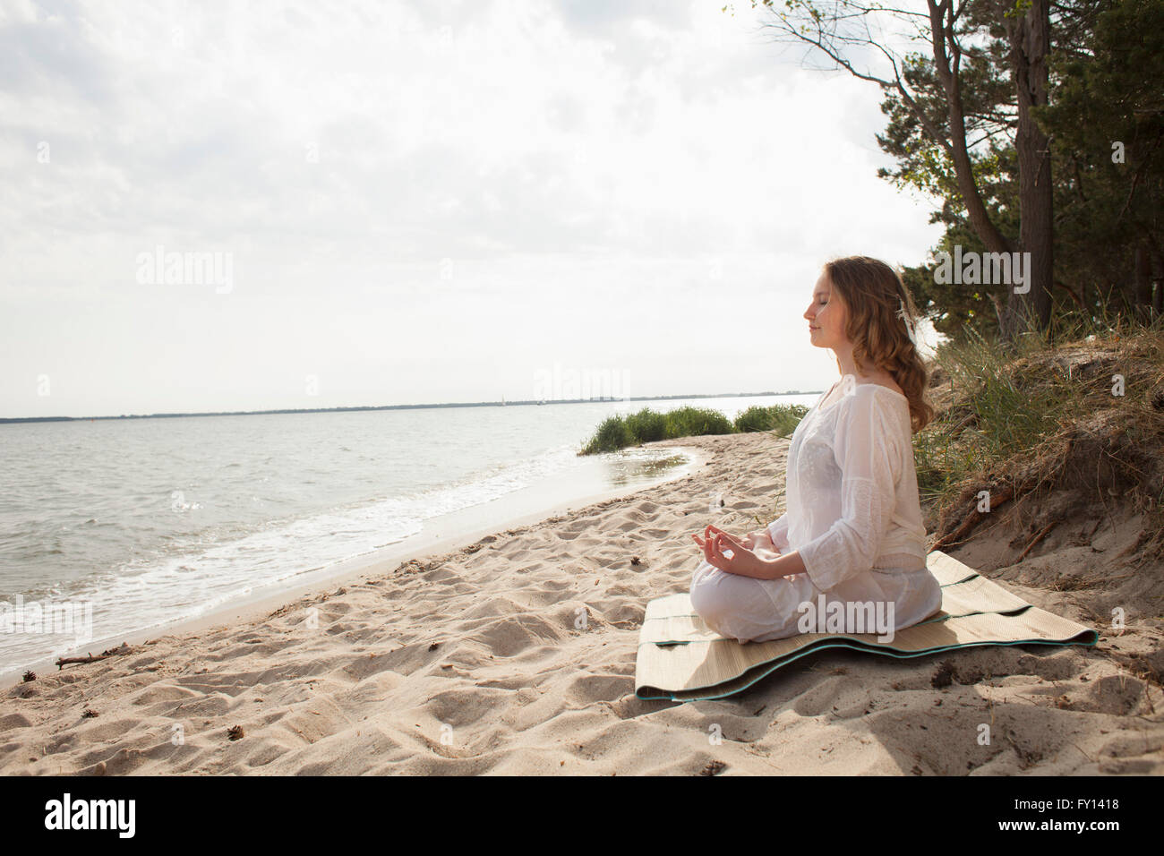 Woman meditating on sea shore at beach against sky Stock Photo - Alamy