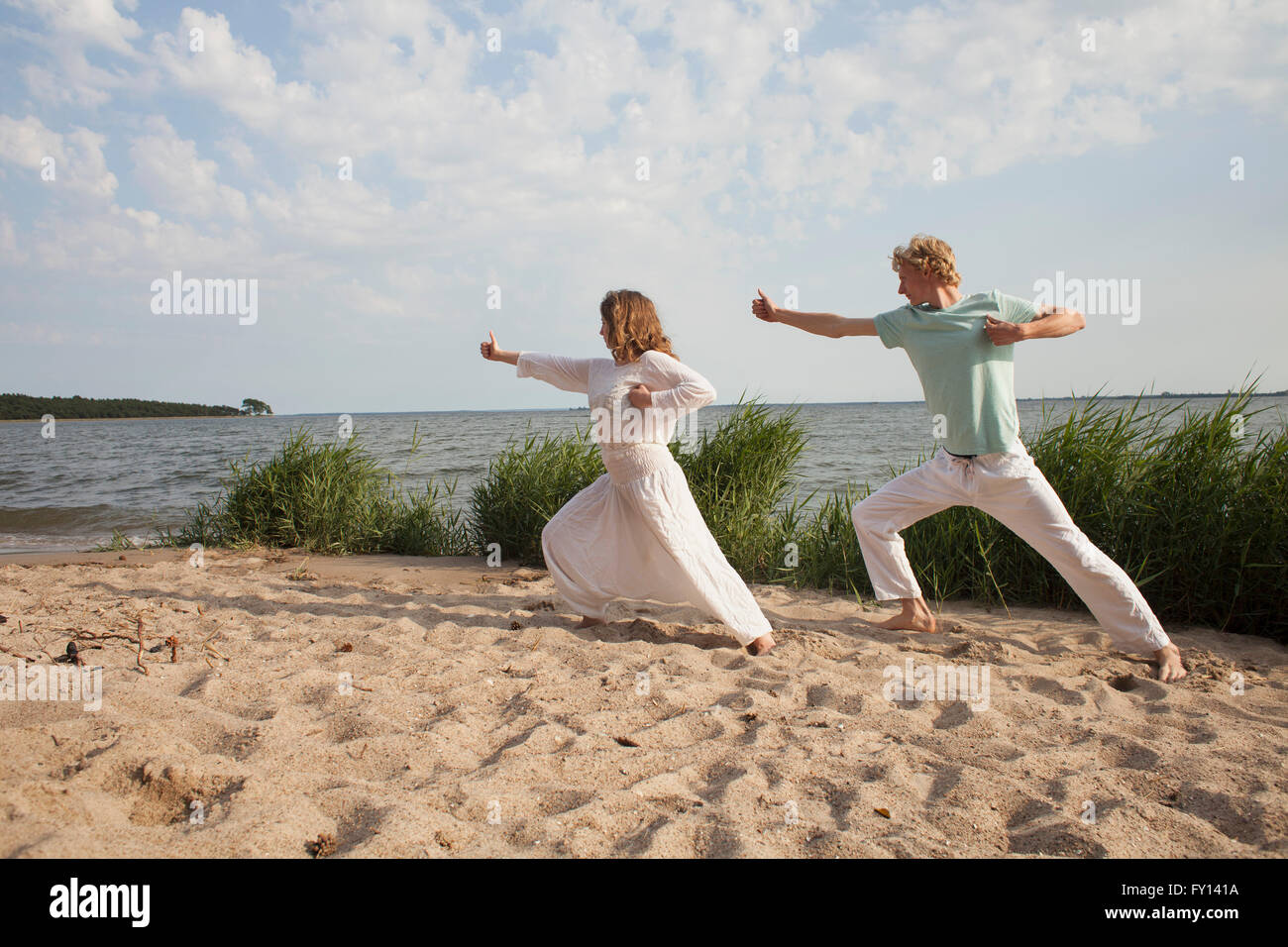 Friends practicing yoga on sea shore at beach against sky Stock Photo