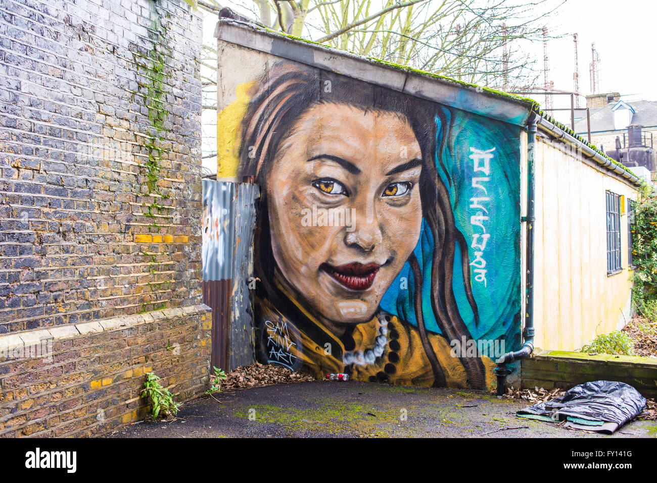 Mural graffiti representing a smiling Asian girl painted on the wall of a small building. Brick wall on the side. Stock Photo