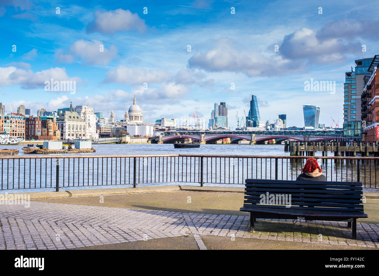 Tourist sitting down on a bench admiring iconic London view from the South Bank with river Thames, Stock Photo