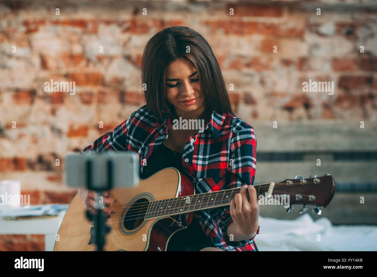 Smart phone in monopod with woman playing guitar at home Stock Photo