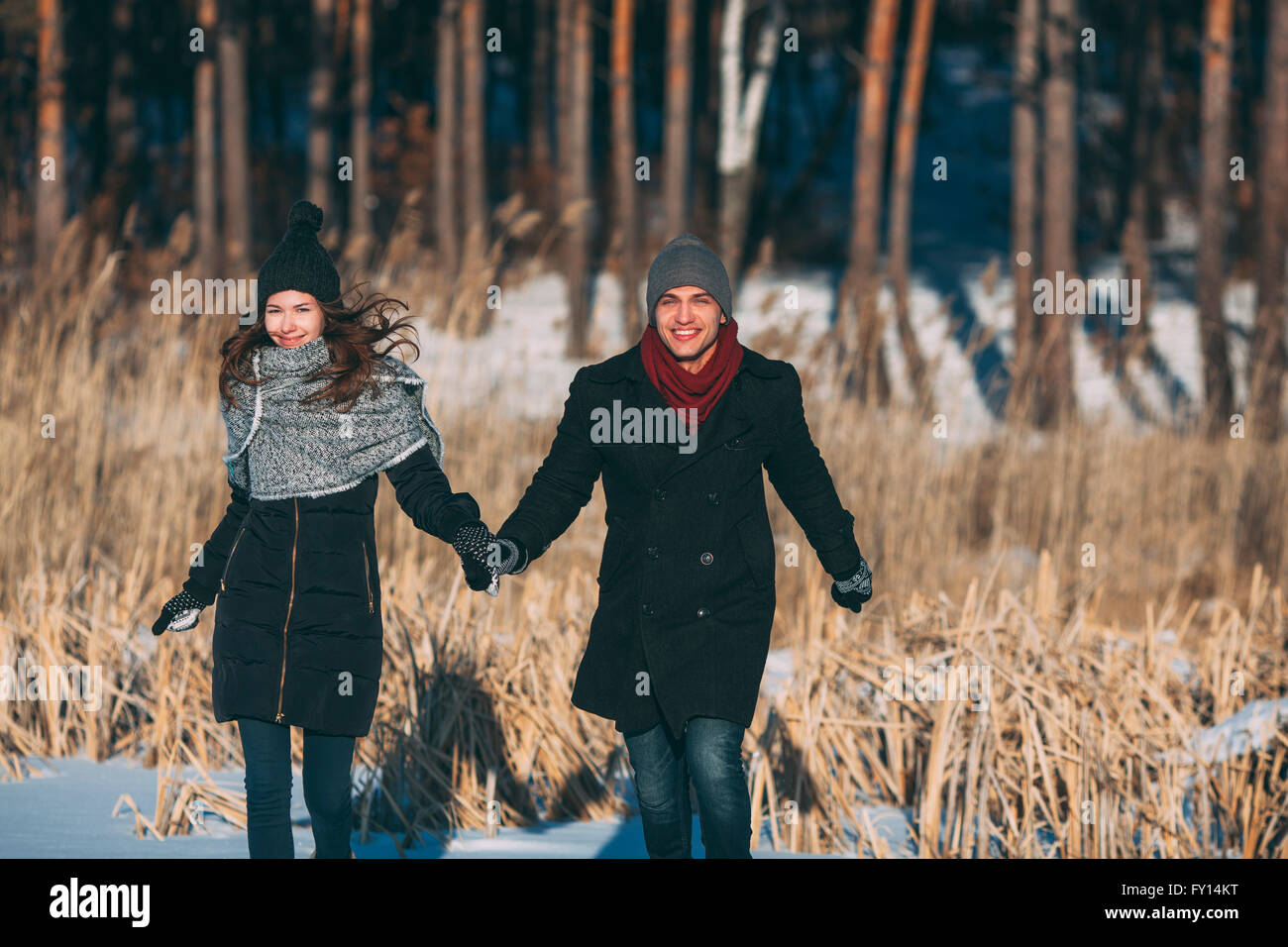 Happy couple holding hands while walking on snow covered field Stock Photo