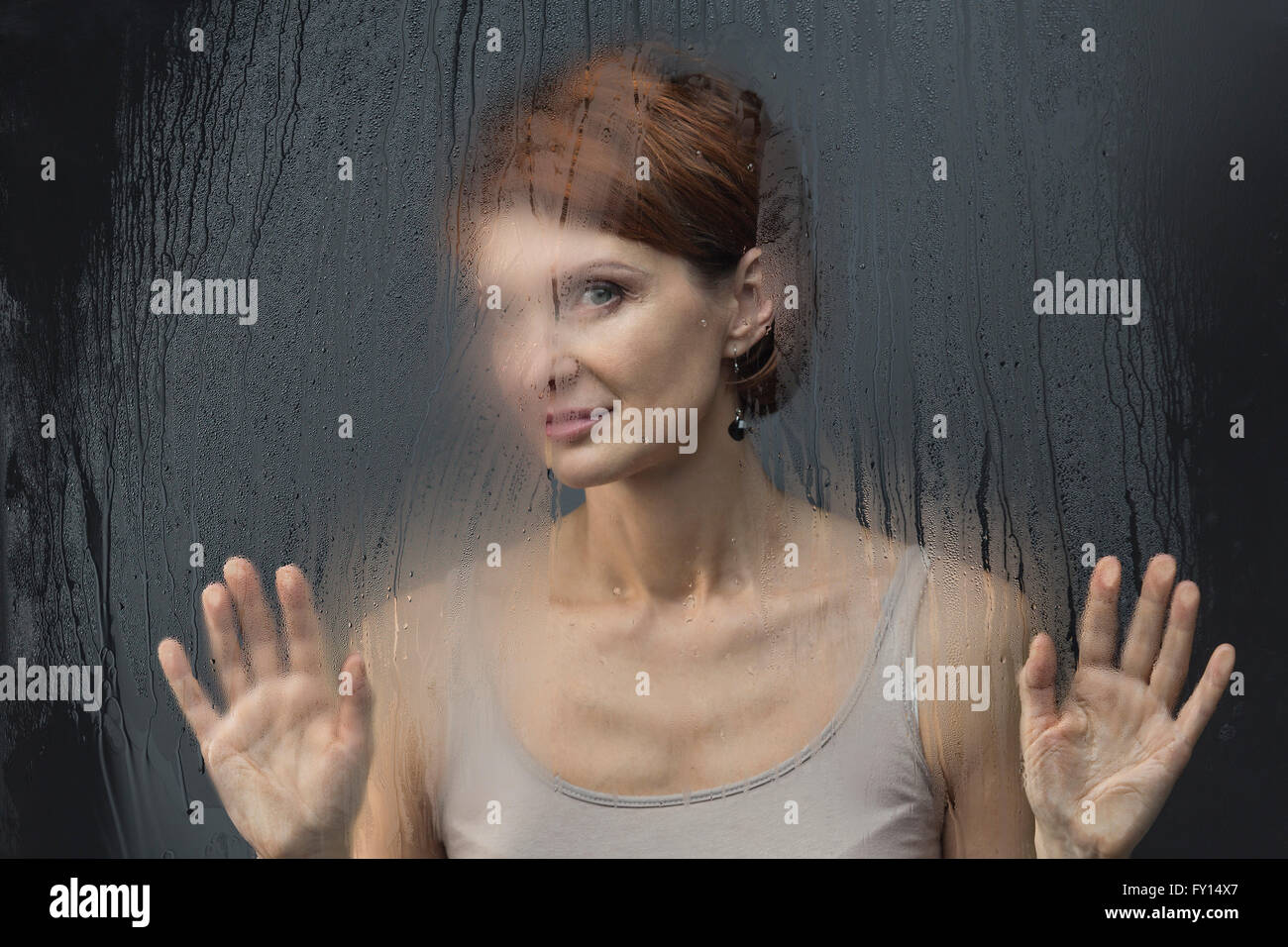 Beautiful woman standing in front on condensed glass against black background Stock Photo