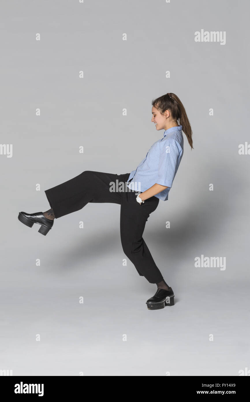 Young woman standing on one leg against gray background Stock Photo